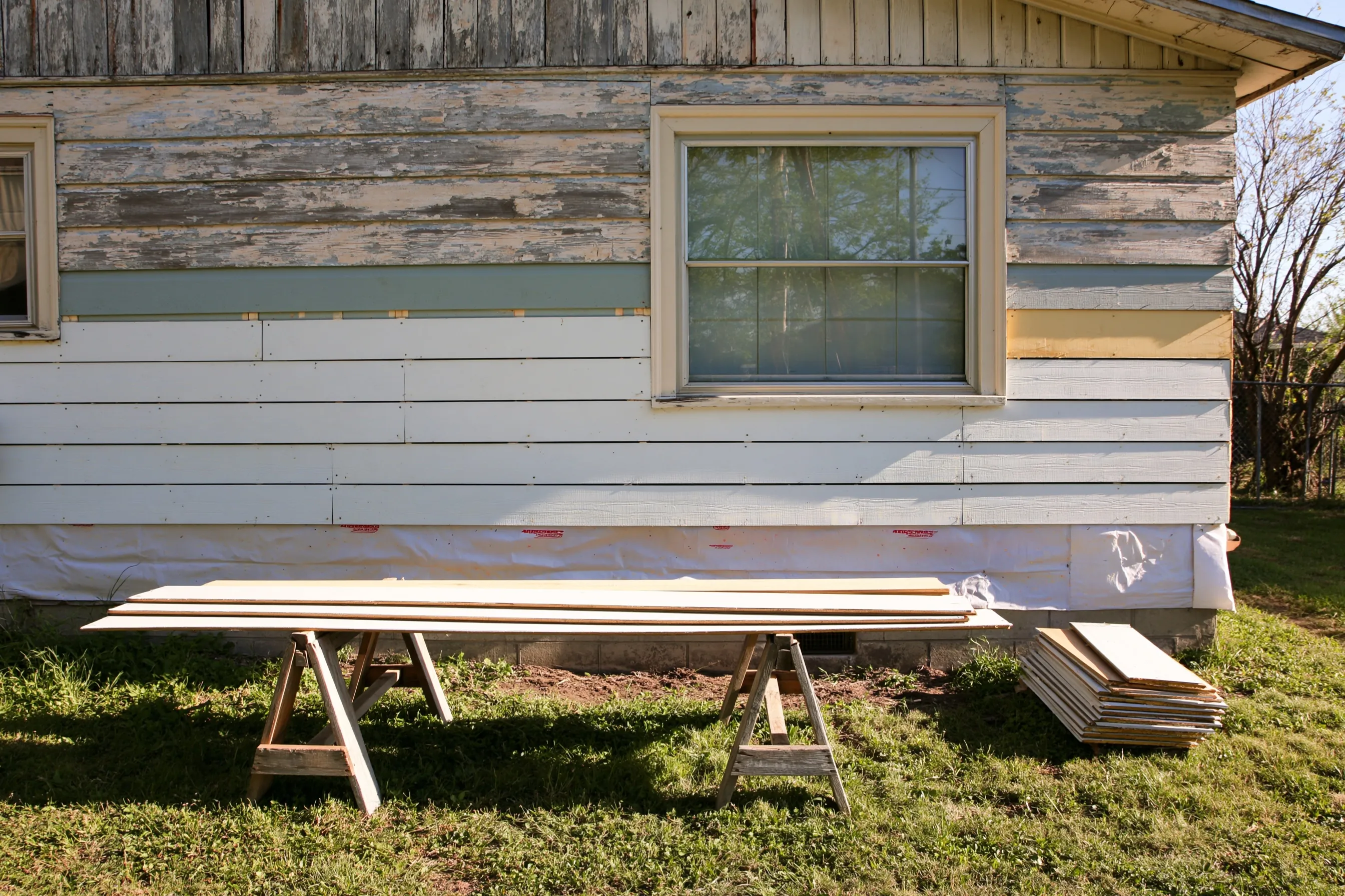 New primed lap boards going on across the lower wall of an old painted wood house